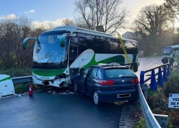 Los bomberos sacan por el techo a tres pasajeros de un bus escolar que chocó con un turismo
